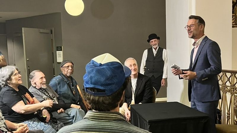 Seated group of people on the left watching FX the magician standing on the right.