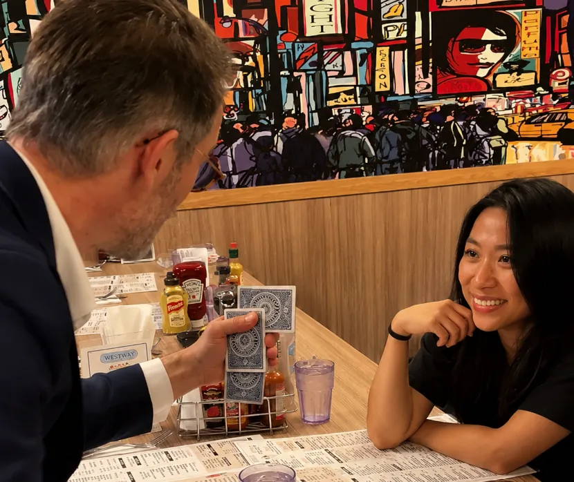 Magician performing a close-up card trick for a guest seated at a restaurant table