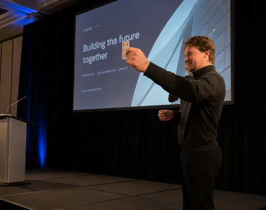 Magician performing a card reveal on a corporate stage with presentation screen