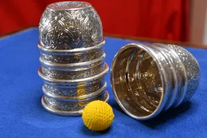 Engraved silver cups and yellow ball used in a classic cups-and-balls magic routine