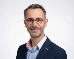 Portrait of FX, the Elegant Magic Artist, wearing a navy jacket and glasses against a white background