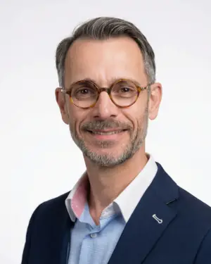 Portrait of FX, the Elegant Magic Artist, wearing a navy jacket and glasses against a white background
